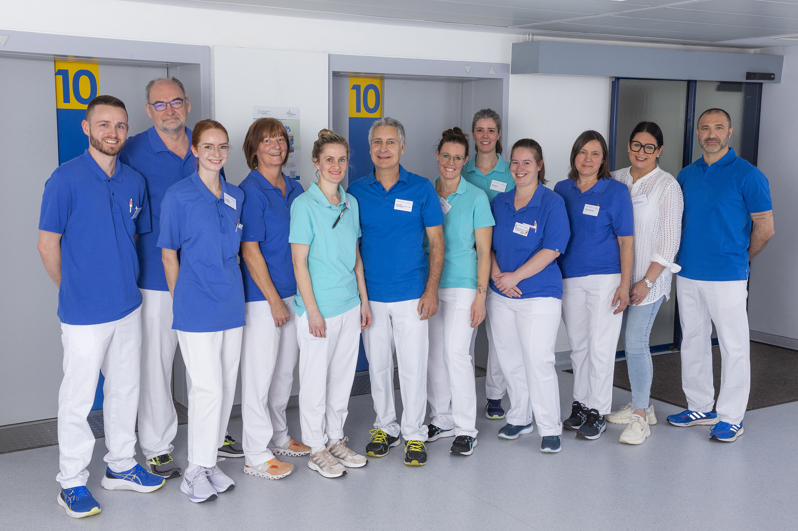 Physiotherapie-Team, mehrere Personen in weißen Hosen und blauen Polo-Shirts in einem Flur
