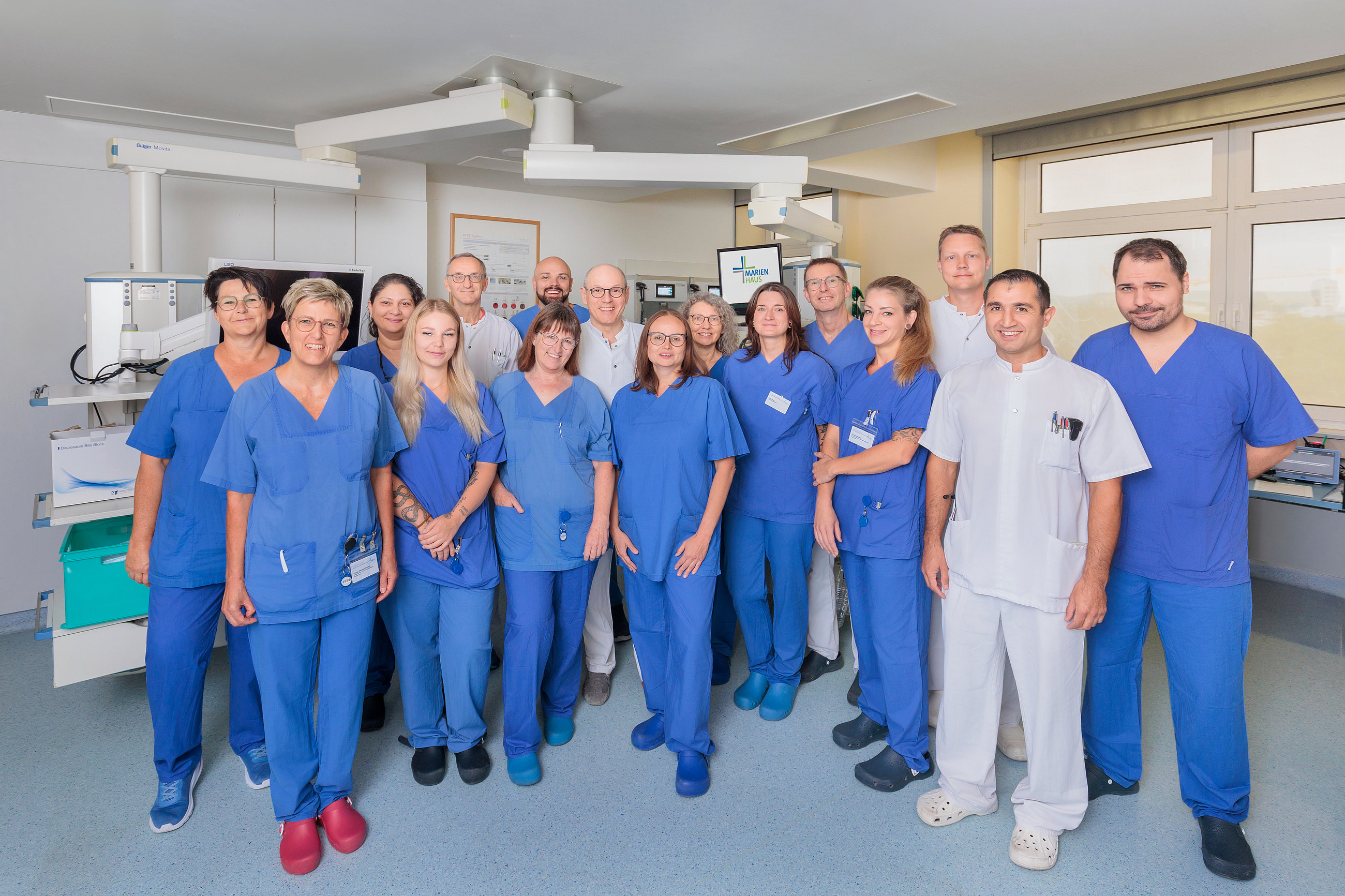 Gruppe von medizinischem Personal in blauen und weißen Kitteln in einem Behandlungsraum