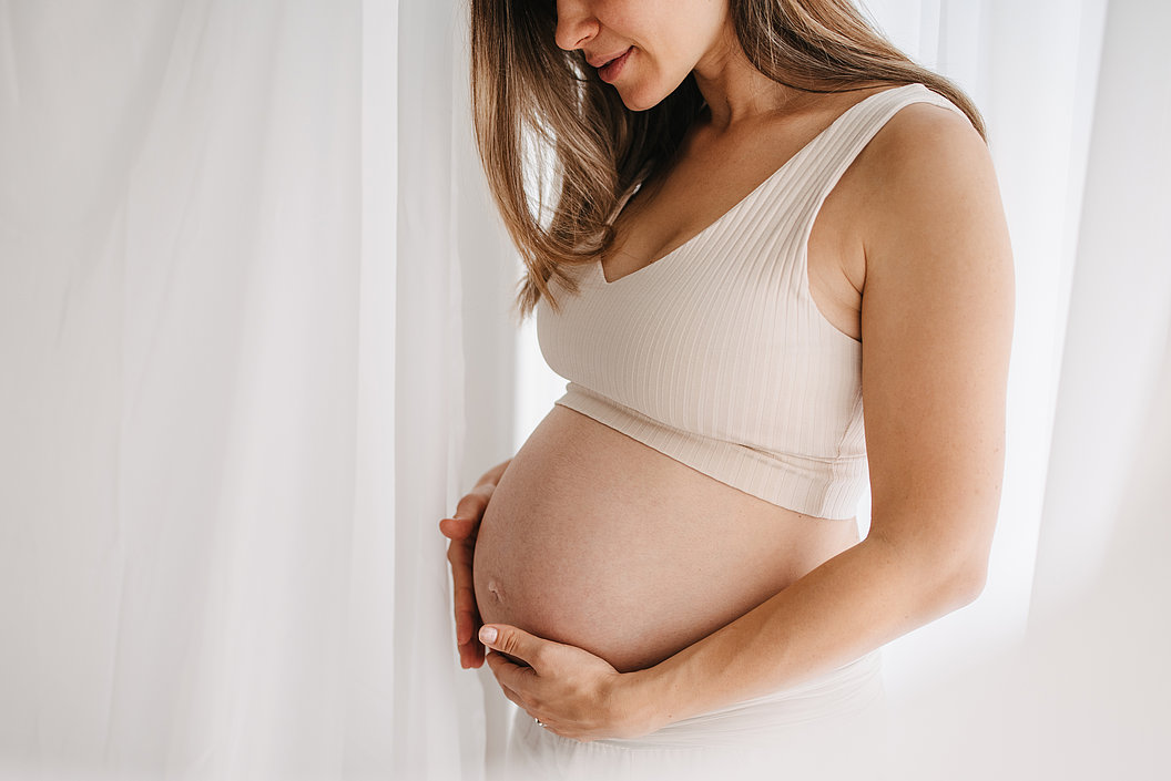 Schwangere Frau in weißem Top hält ihren Bauch und lächelt leicht