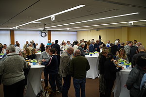 Menschen stehen in einem großen Raum an Stehtischen und unterhalten sich bei einer Veranstaltung