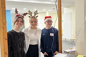 Drei Personen mit Weihnachtsaccessoires stehen hinter einem Tresen mit Waffeln und Verpackungen in einem hellen Raum