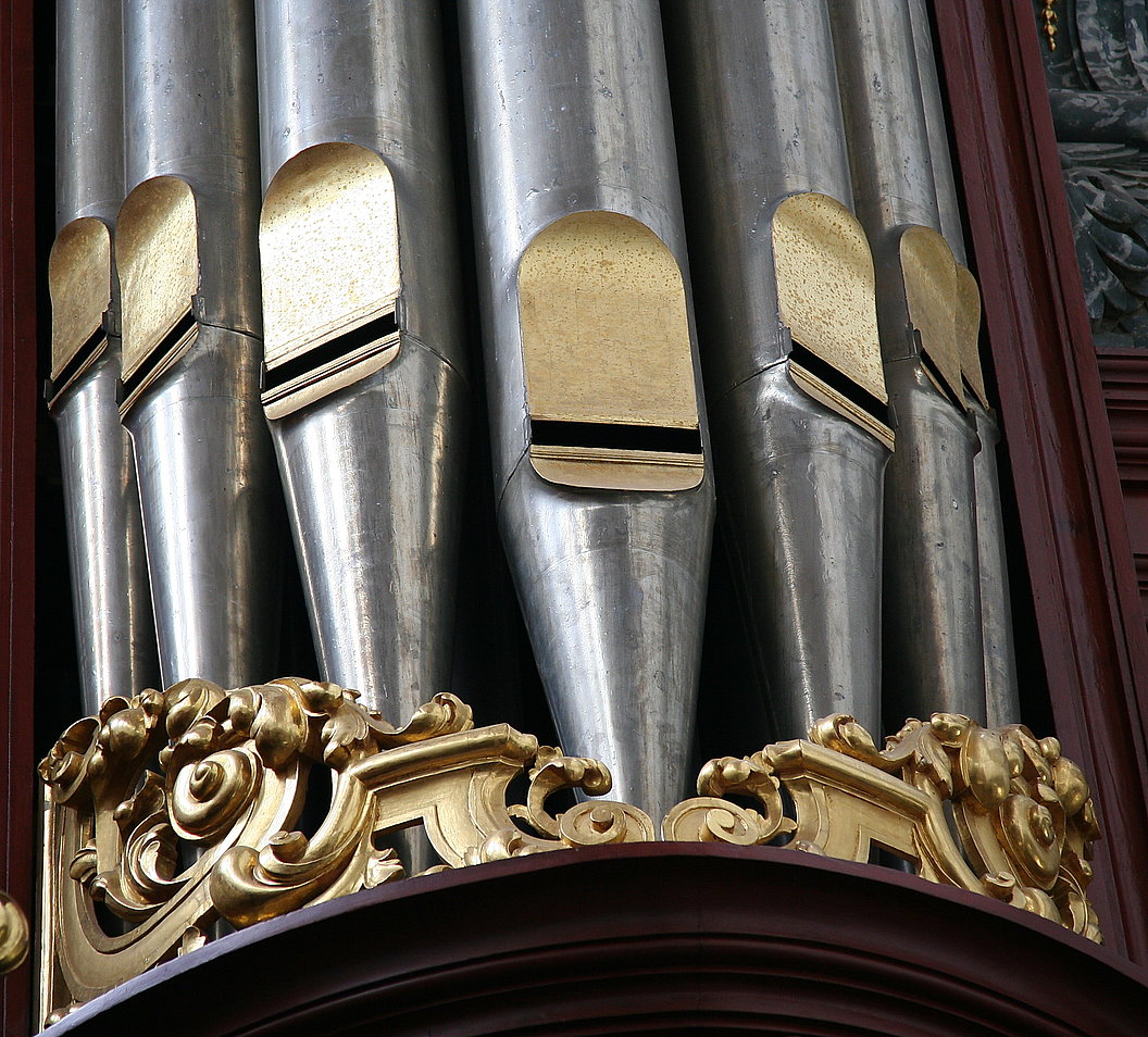 Nahaufnahme von verzierten Metallpfeifen einer Orgel mit goldfarbenen Verzierungen am unteren Rand