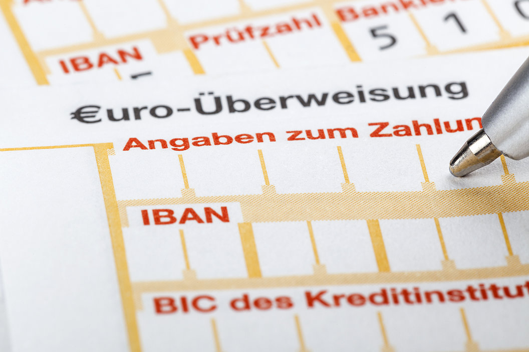 Ausschnitt eines SEPA-Überweisungsformulars mit sichtbaren Feldern für IBAN, BIC und Angaben zum Zahlungsempfänger; eine Stiftspitze zeigt auf das Formular. 