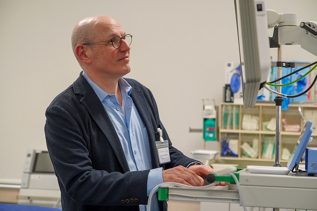 Mann mit Brille und Sakko bedient in Laborumgebung ein Gerät mit Monitor und Steuerungselementen