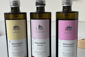 Drei Flaschen Massageöl mit Pumpverschluss in den Sorten Honig-Ingwer, Waldrose und Lavendel-Malve nebeneinander auf weißem Untergrund