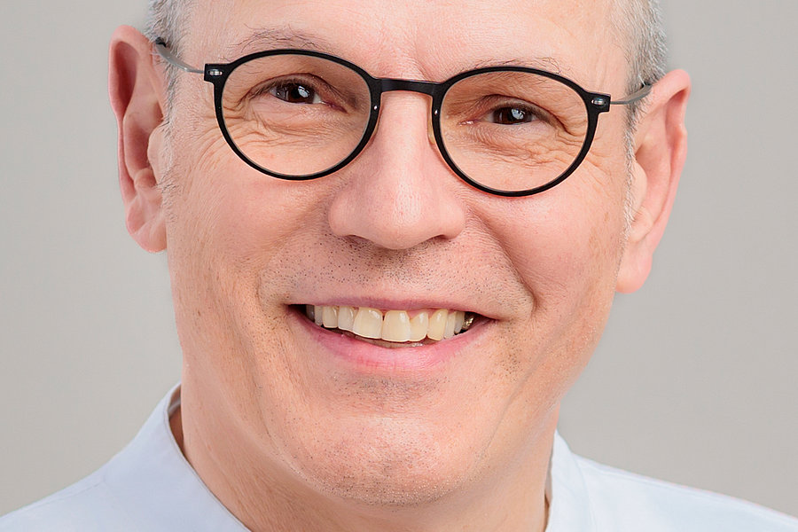 Dr. Eric-Thorsten Steinheim in dunklem Anzug, hellblauem Hemd und dunkelroter Krawatte mit Muster.