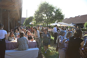 Menschen sitzen und stehen bei einer sonnigen Gartenparty mit Tischen, weißen Sonnenschirmen und Bäumen