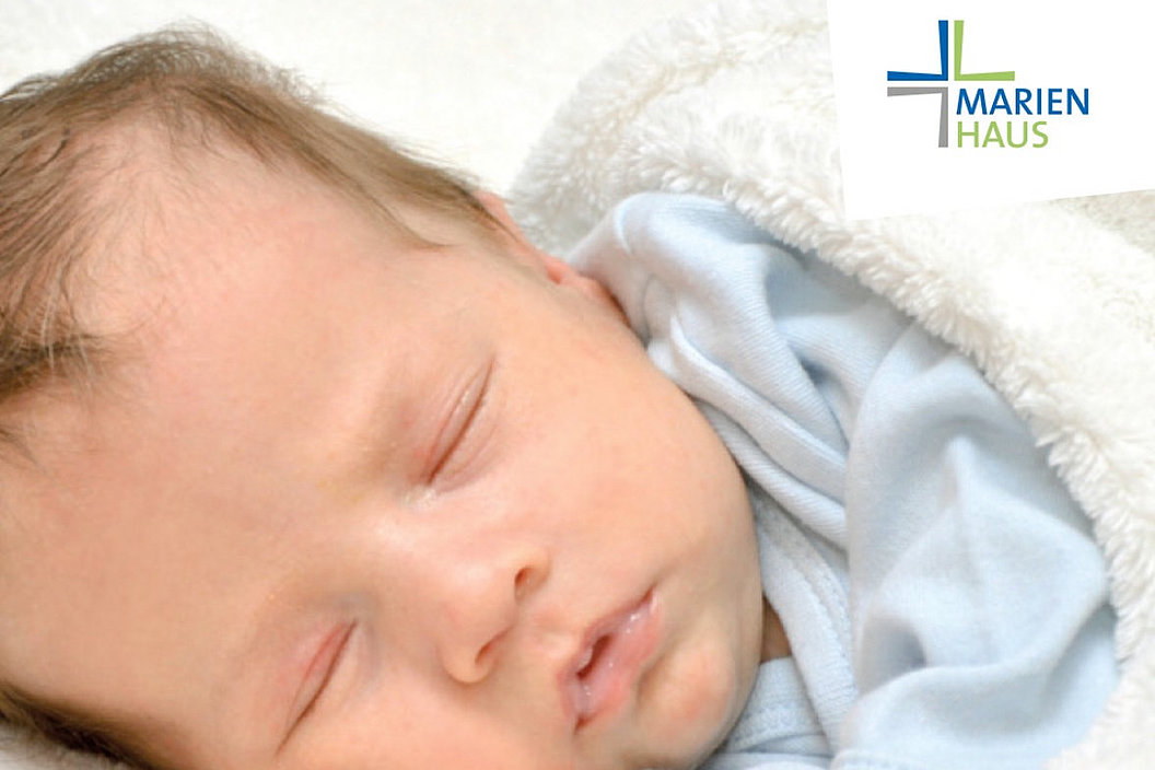 Baby in blauem Strampler liegt auf weißer Decke, rechts oben Logo mit Schrift 'MARIENHAUS' und farbigem Kreuz