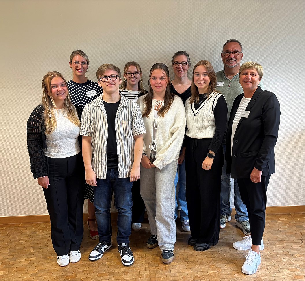 Gruppe von zehn Personen steht in einem Raum mit hellem Hintergrund, trägt lässige und formelle Kleidung