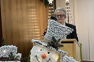 Drei beleuchtete Schneemannfiguren mit schwarzen Hüten und orangefarbenen Nasen stehen vor einem Rednerpult in einem Raum mit Holzvertäfelung und Weihnachtsdeko.