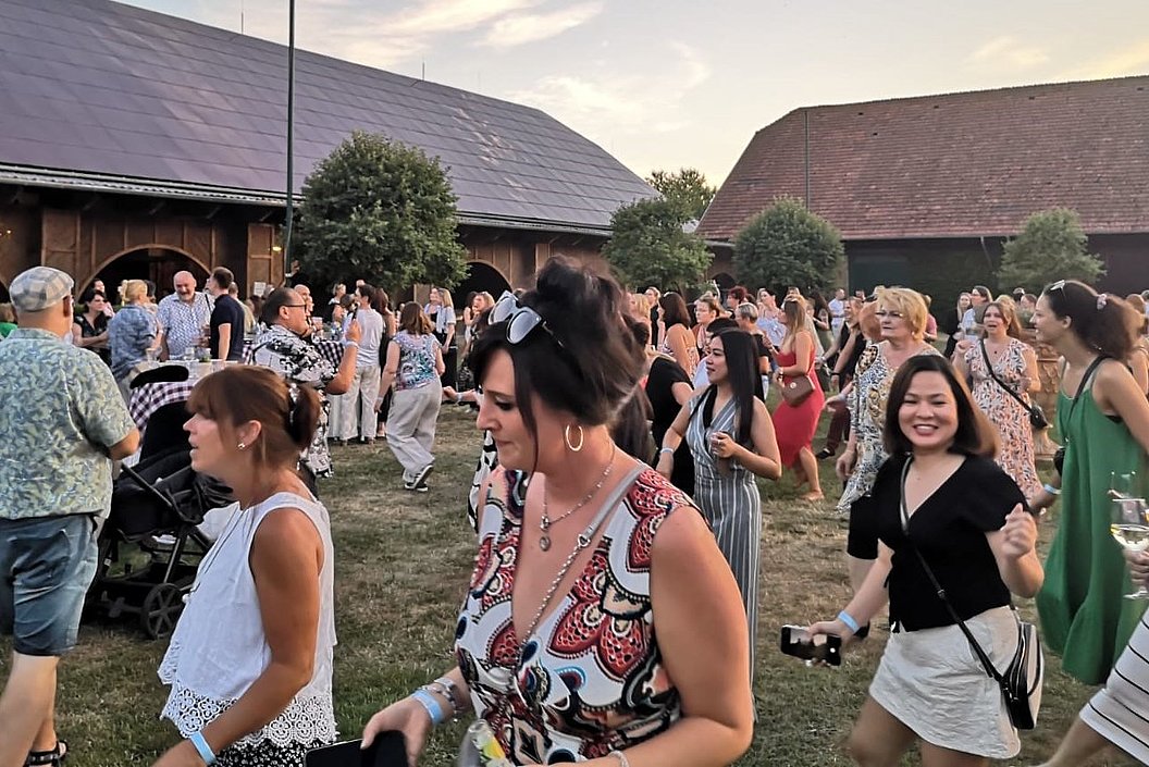 Menschen bei einer Gartenparty oder Veranstaltung im Freien vor zwei großen Scheunen bei Sonnenuntergang