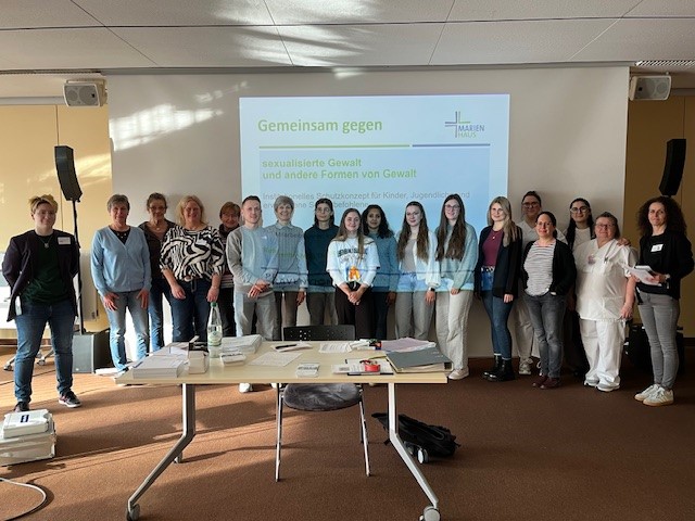 Gruppenfoto von Teilnehmern einer Veranstaltung zu Gewaltprävention im Raum mit Präsentation im Hintergrund.